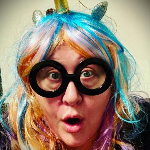 Melanie in a rainbow wig and unicorn headband with silly glasses.
